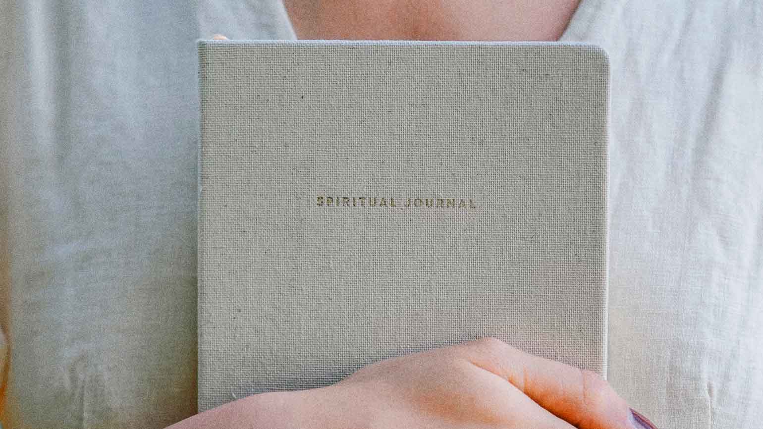 Woman holding a white spiritual journal that holds her spiritual goals
